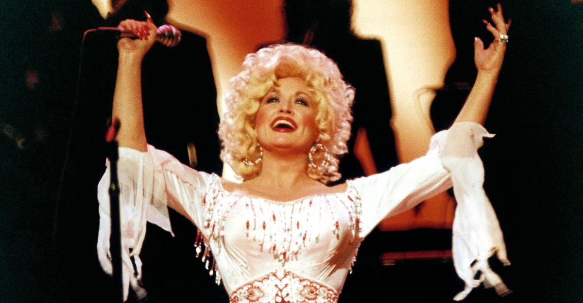 Dolly Parton on stage, arms raised, from The Atlantic’s piece on her style.