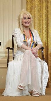 Color photograph of Dolly Parton seated at the White House on 3 December 2006, wearing a pale gown and the Kennedy Center Honors ribbon.